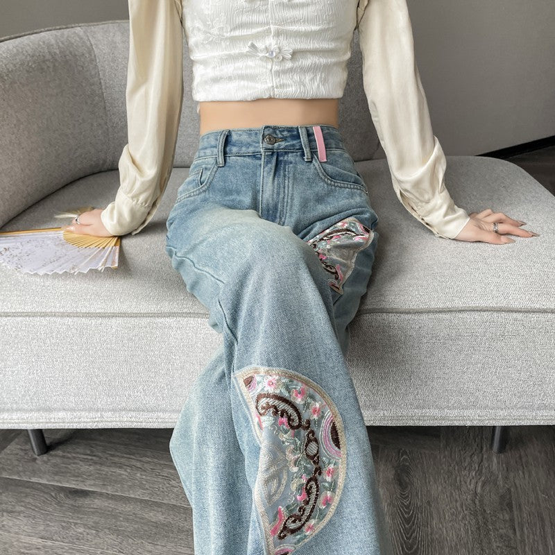 Glacier-blue jeans with embroidered patterned panels at the thigh and lower leg.