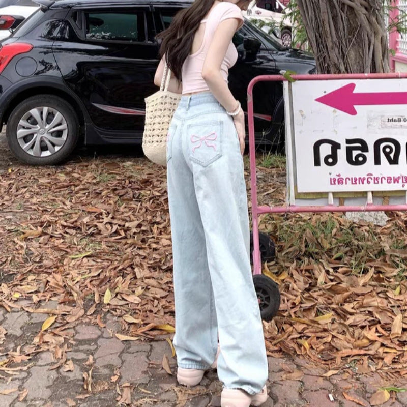 Rear view of light-blue wide-leg jeans with pink embroidered bows on the back pockets.